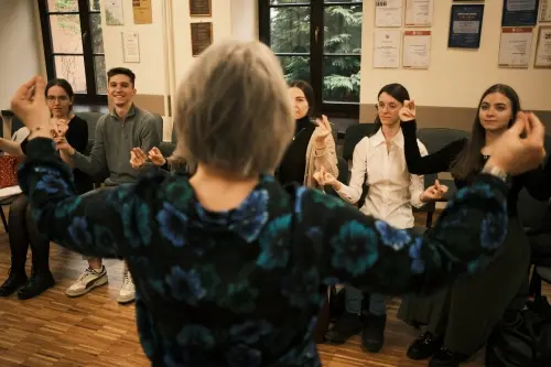 Zajęcia z edukacji muzycznej - grupa uśmiechniętych osób. Na pierwszym planie odwrócona tyłem dyrygentka.